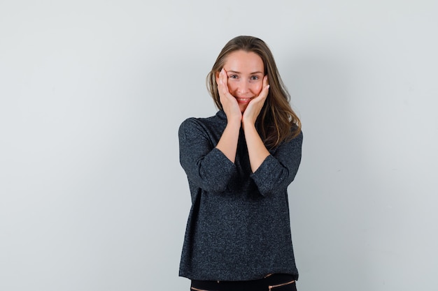 Gratis foto jonge vrouw in overhemd hand in hand op wangen en op zoek vrolijk