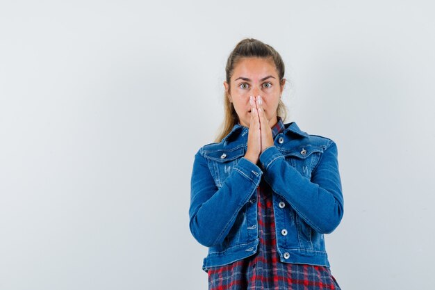 Jonge vrouw in overhemd, jasje hand in hand in biddend gebaar en op zoek verrast, vooraanzicht.