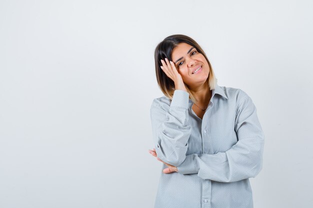 Jonge vrouw in oversized shirt die het gezicht aan de kant dempt en er gelukkig uitziet, vooraanzicht.