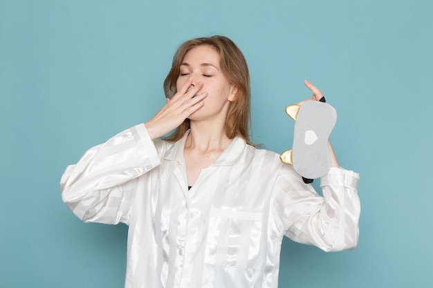 jonge vrouw in pyjama's en slaapmasker geeuwen op blauw