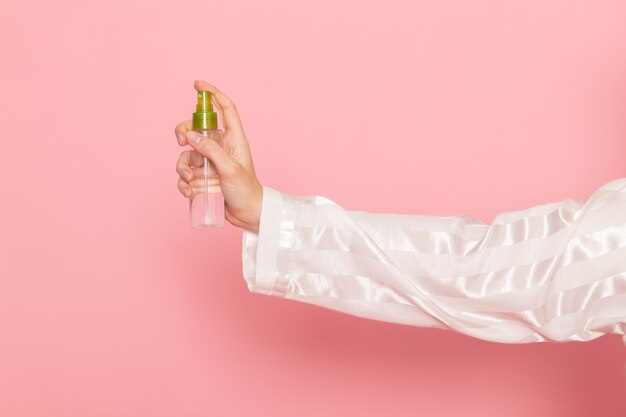 jonge vrouw in pyjama's en slaapmasker met make-up spray op roze
