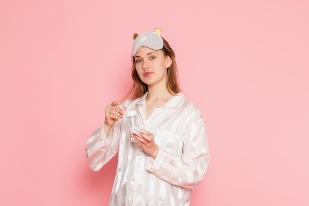 jonge vrouw in pyjama's en slaapmasker poseren en houden make-up spray op roze