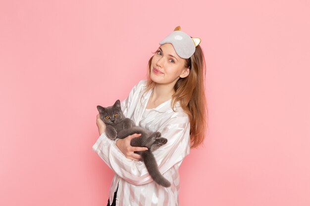 jonge vrouw in pyjama's en slaapmasker poseren met kitten op roze