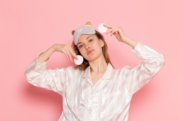 jonge vrouw in pyjama's en slaapmasker schoonmaken van haar gezicht op roze