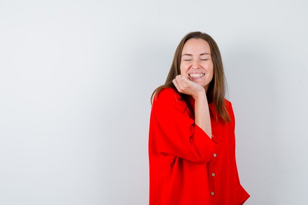 Jonge vrouw in rode blouse leunende kin bij de hand en op zoek gelukkig, vooraanzicht.