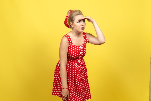 Gratis foto jonge vrouw in rode polka dot jurk afstand kijken op geel