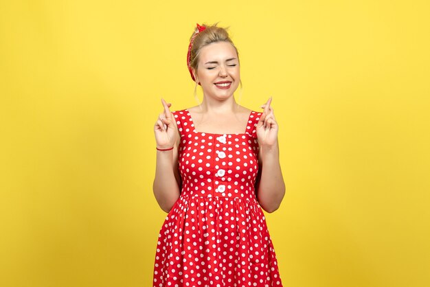 jonge vrouw in rode polka dot jurk kruisen haar vingers op geel