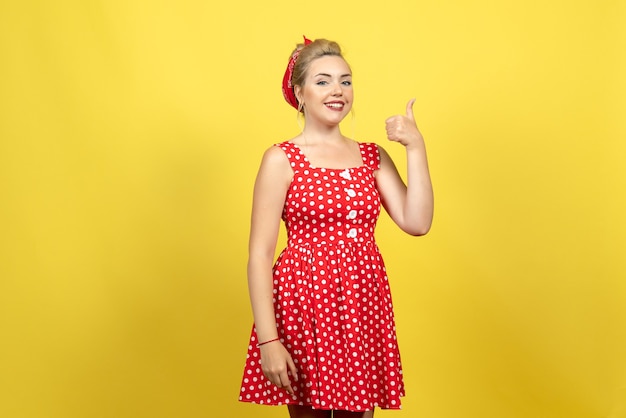 jonge vrouw in rode polka dot jurk poseren en lachend op geel