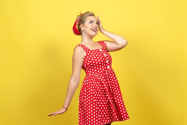 Gratis foto jonge vrouw in rode polka dot jurk poseren op geel