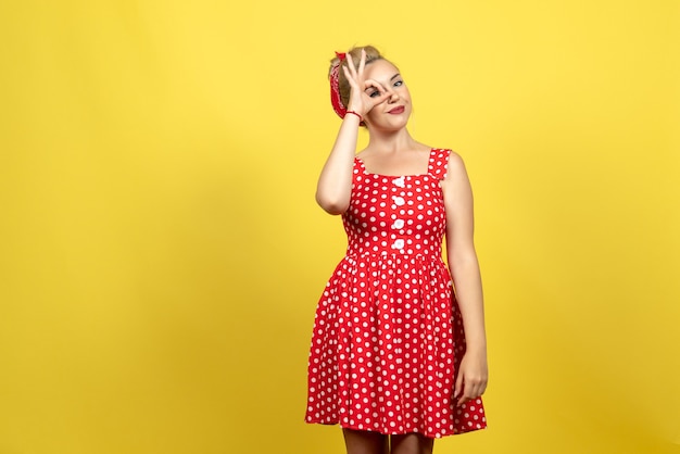 Gratis foto jonge vrouw in rode polka dot jurk poseren op gele vloer jurk vrouw mode oude kleur retro