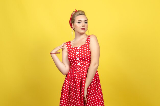 jonge vrouw in rode polka dot jurk staan en poseren op geel