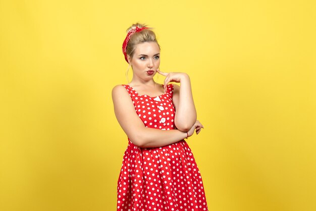 Gratis foto jonge vrouw in rode polka dot jurk staan en poseren op geel