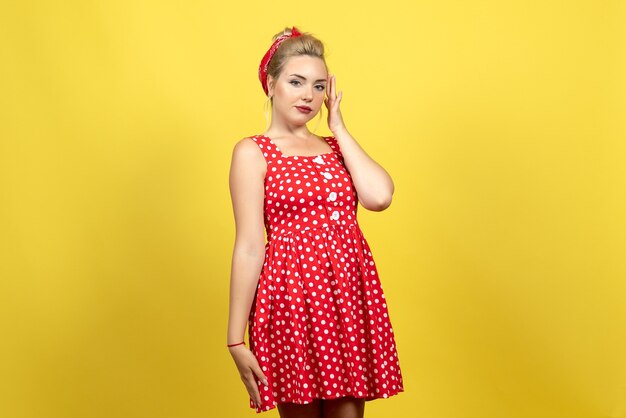 jonge vrouw in rode polka dot jurk staan en poseren op geel