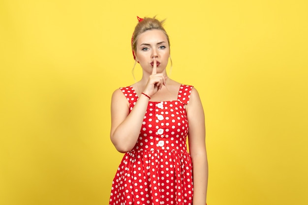 jonge vrouw in rode polka dot jurk vragen stil te zijn op geel