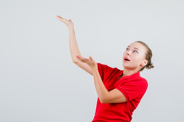 Jonge vrouw in rode t-shirt die palmen opheft om iets vast te houden en verbaasd kijkt