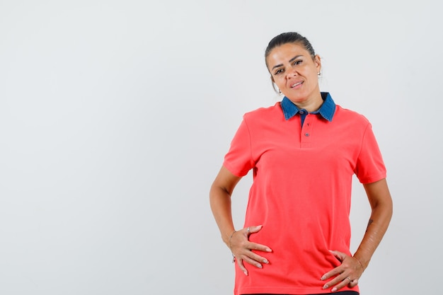 Jonge vrouw in rode t-shirt hand in hand op buik en op zoek naar mooi, vooraanzicht.