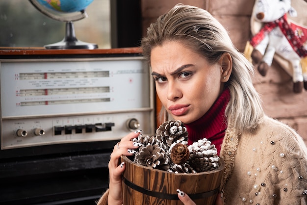 Jonge vrouw in rode trui met een houten mand vol dennenappels