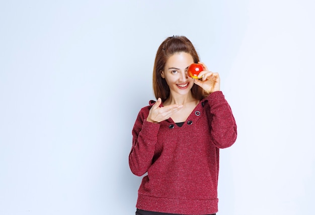 Jonge vrouw in rood jasje die een rode appel aan haar oog houdt
