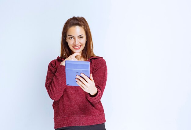 Jonge vrouw in rood jasje die iets op een blauwe rekenmachine berekent en er verward uitziet