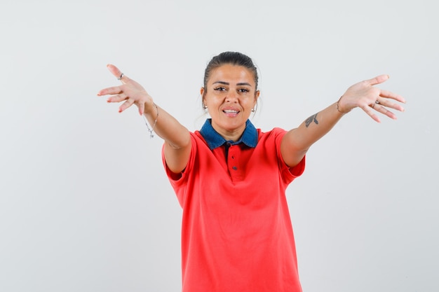 Jonge vrouw in rood t-shirt handen uitrekken als uitnodigend om te komen en op zoek beminnelijk, vooraanzicht.