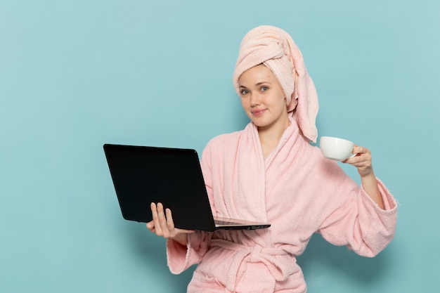 jonge vrouw in roze badjas na douche koffie drinken en met behulp van laptop lachend op blauw