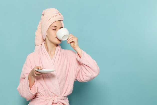 jonge vrouw in roze badjas na douche koffie drinken op blauw