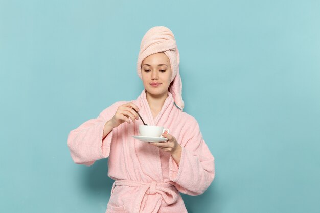 jonge vrouw in roze badjas na douche koffie mengen op blauw
