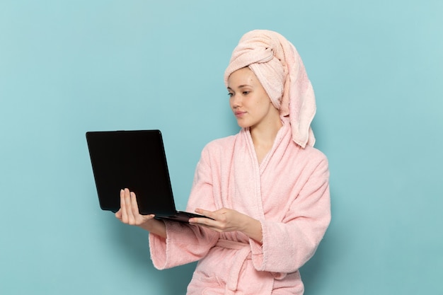 jonge vrouw in roze badjas na douche met laptop op blauw