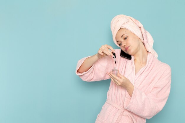 jonge vrouw in roze badjas na douche praten over telefoon haar nagels schilderen op blauw