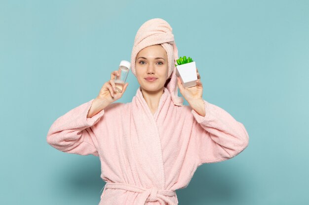 jonge vrouw in roze badjas na het douchen met groene plantenspray op blauw