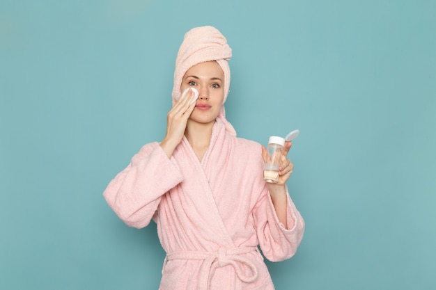 jonge vrouw in roze badjas na het douchen met make-up reiniger op blauw