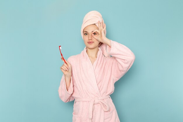 jonge vrouw in roze badjas na het douchen met tandenborstel op blauw