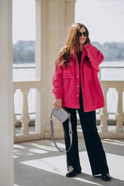 Jonge vrouw in roze jas die op straat staat