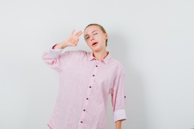 Jonge vrouw in roze overhemd die ok teken en oog knipogen tonen