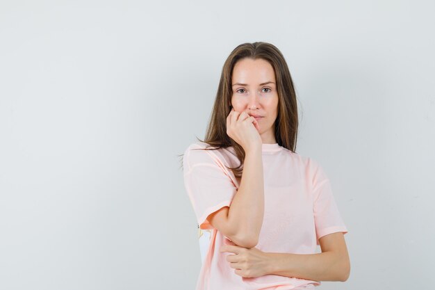 Jonge vrouw in roze t-shirt staande in denken pose en op zoek verstandig, vooraanzicht.