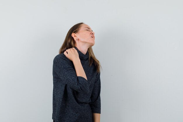 Jonge vrouw in shirt die aan nekpijn lijdt en vermoeid kijkt