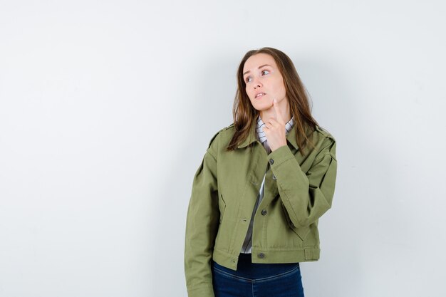 Jonge vrouw in shirt, jas met vinger op kin en peinzend, vooraanzicht.