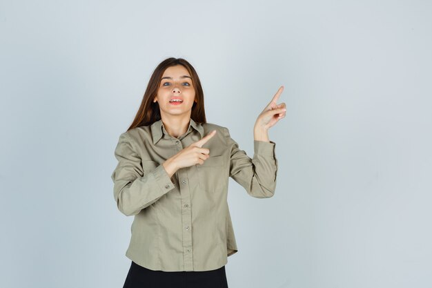 Jonge vrouw in shirt, rok wijzend naar de rechterbovenhoek en vrolijk, vooraanzicht.