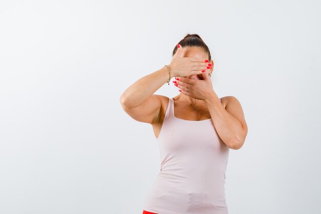 Jonge vrouw in singlet gezicht sluiten met handen en op zoek mooi, vooraanzicht.