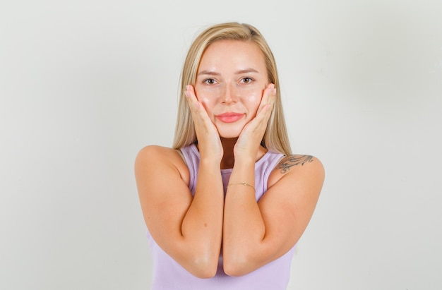 Jonge vrouw in singlet, minirok hand in hand op wangen en glimlachen