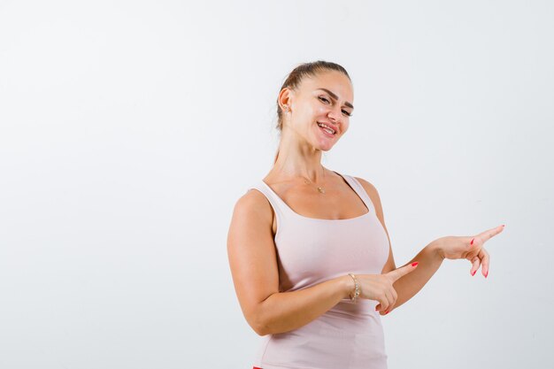 Jonge vrouw in singlet wijst naar de rechterkant en ziet er vrolijk uit, vooraanzicht.