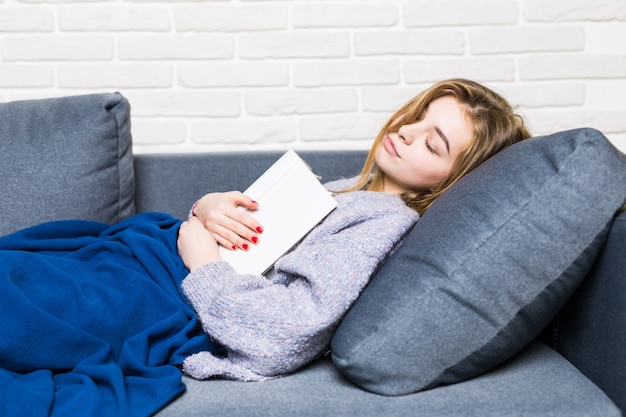 Jonge vrouw in slaap gevallen tijdens het lezen liggend op haar rug in het bed met haar boek op haar buik