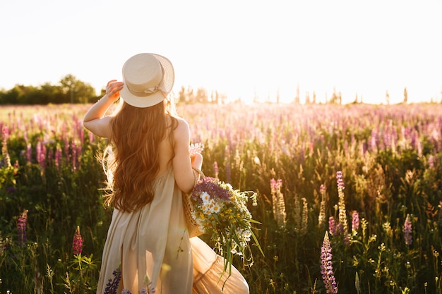 Jonge vrouw in strohoed en kleding met boeket van lupinebloemen