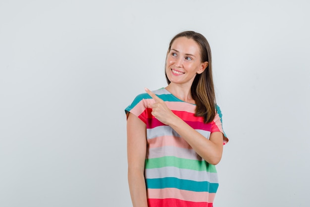 Jonge vrouw in t-shirt die naar kant wijst en vrolijk, vooraanzicht kijkt.