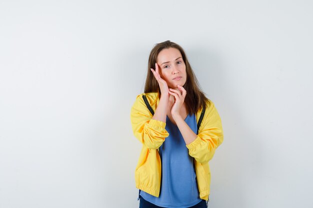 Jonge vrouw in t-shirt, jas die de huid op haar wang aanraakt en er aantrekkelijk uitziet, vooraanzicht.