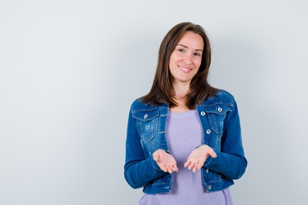 Jonge vrouw in t-shirt, jas die open handen toont en er vrolijk uitziet, vooraanzicht.