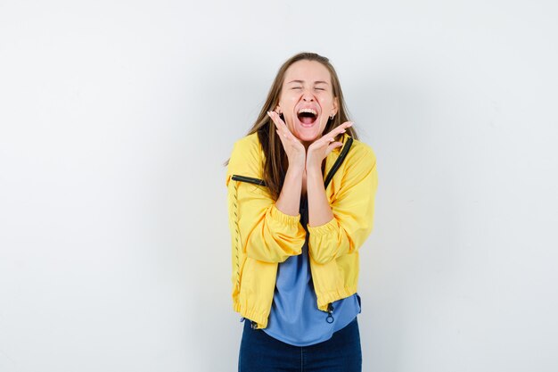 Jonge vrouw in t-shirt, jas hand in hand onder de kin en ziet er gelukkig uit, vooraanzicht.