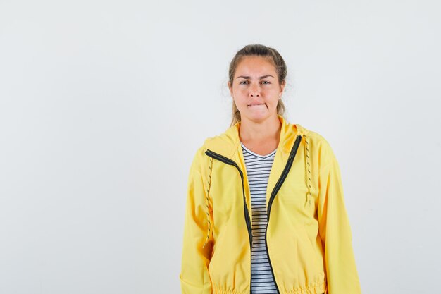 Jonge vrouw in t-shirt, jasje op haar lip bijten en op zoek verstandig, vooraanzicht.