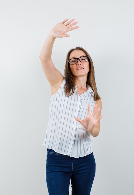 Jonge vrouw in t-shirt, jeans met opgeheven handpalmen en op zoek grappig, vooraanzicht.