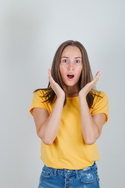 Jonge vrouw in t-shirt, korte broek, hand in hand in de buurt van gezicht en op zoek verbaasd